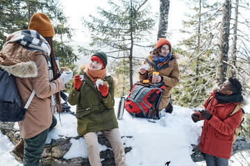 Group of active young Black and Caucasian friends spending weekend together in mountains on sunny winter day having lunch break