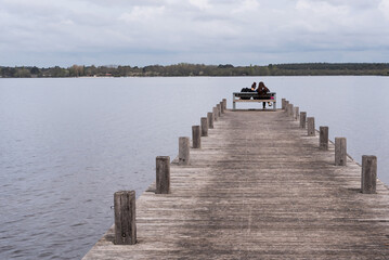 Naklejka premium Two young women sitting on a bench on a pier at the Pond of Leon. Landes