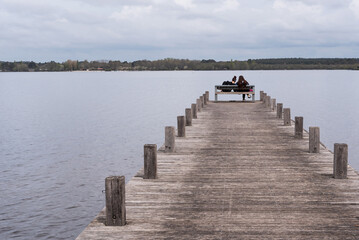 Two young women sitting on a bench on a pier at the Pond of Leon. Landes