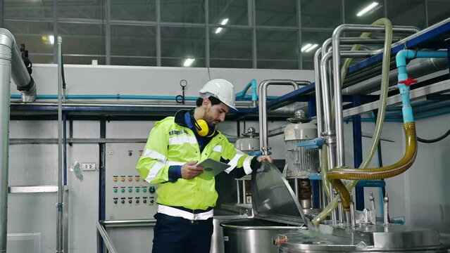Mechanical engineer with tablet checking condition of storage tank and pipeline for observe abnormal operating status in beverage production plant
