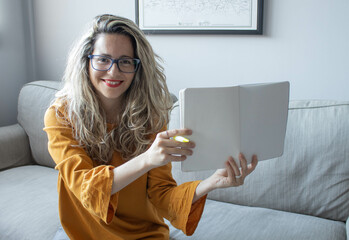 Blonde girl sitting on a sofa while showing a notebook. Concept: education.