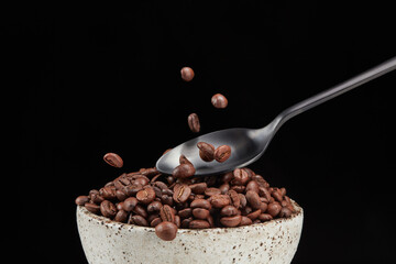 Putting coffee beans from a spoon in a bowl on a black background. Shallow depth of field