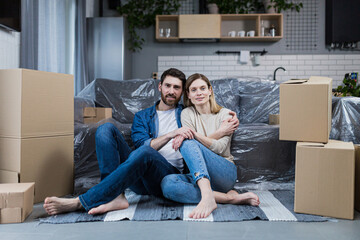 Happy young couple man and woman at home sitting on sofa in new rented apartment, near cardboard boxes