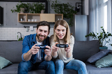 Obraz premium Happy couple man and woman playing game using joystick while sitting on sofa at home