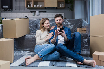 A man and a woman in a new apartment, a married couple sitting on the floor, near cardboard boxes,...