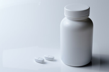 white plastic medicine jar and two white pills. light background