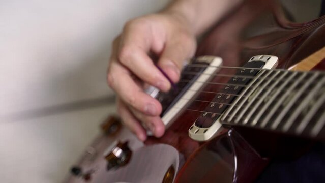 humbucker electric guitar pickup close-up on a varnished beautiful brown electric guitar. defocused white hand of a guitarist playing with a plastic plectrum arpeggio on metal strings