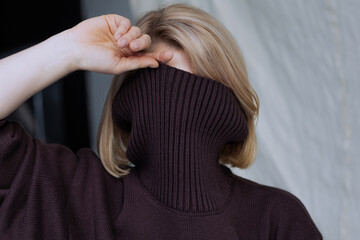 A teenager girl covered her face with a brown knitted sweater, hid from society and other people's...