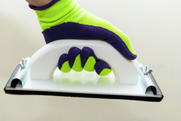Plaster float in male hand in bright glove against a gray wall. Plastering grater in the hands of a...