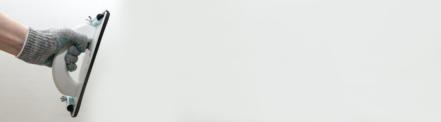 Plaster float in male hand in glove against a gray wall. Plastering grater in the hands of a...