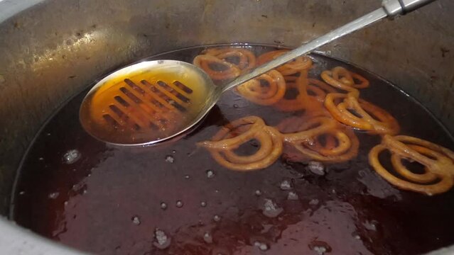 Raw jilapi deep frying 4k video clip.Jilapi making on a hot big pan.Jalebi, also known as jilapi, jilebi, jilipi, zulbia, jerry, mushabak, or zalabia, is a popular Indian sweet snack.