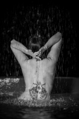 attractive naked woman with tattoos on her back bathing in the rain