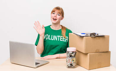 red head pretty woman smiling happily, waving hand, welcoming and greeting you. Donation volunteer...