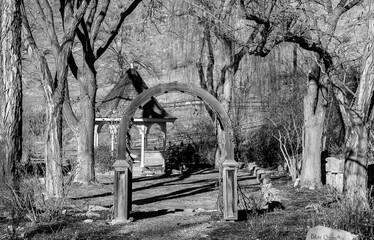 Black and white of Gazebo and archway to garden with trees in wintertime. 