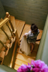 The bride in a bathrobe with a white dress in her hands climbs the stairs.