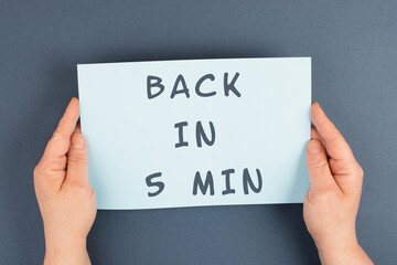 Back in 5 min is standing on a paper, hands hold message, working break, be right back