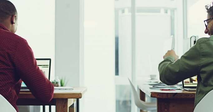 The two of us will make history. Two handsome multi ethnic happy diverse confident young business men fist bumping in celebration while working on their computers at desks in a modern creative office