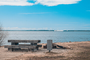 Fototapeta na wymiar A cozy place for a picnic in the summer near a pond - a wooden table, benches and a trash can, near a fire pit, Latvia.