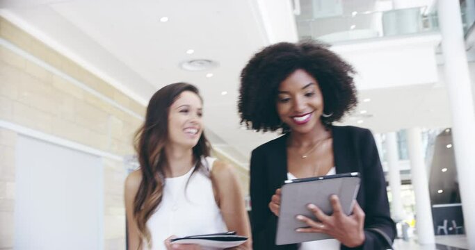 We have a meeting at 2pm. 4k video footage of two confident businesswomen walking together with digital tablets on their hands at work.
