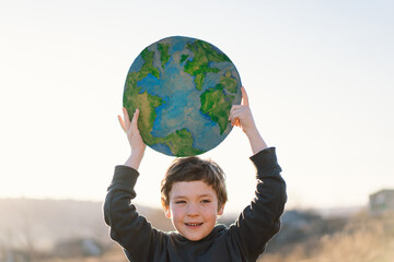 Protection and love of earth. Little boy holding planet in hands against green spring background....