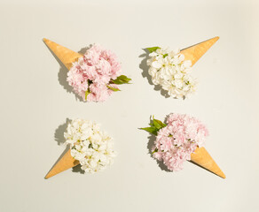  Ice cream cone with white and pink flowers  over a light background, flat lay. Minimalistic spring design.
