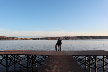 father and daughter stand with their backs to the pier and look at the water