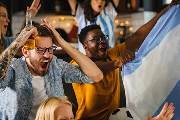 Group of young multi-ethnic people watching a soccer game on a tv at home. Excited multicultural football fans celebrating a goal score of their team