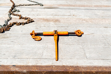 A ratchet load binder and tie down chain on the wooden deck of a flatbed truck tailer. Room for text. - obrazy, fototapety, plakaty