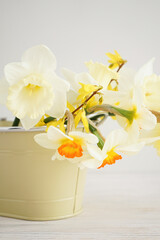 Beautiful bouquet of fresh yellow daffodil flowers in vase against wooden background, close-up. Vertically.