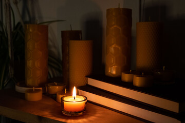 Various beeswax candles are displayed on a shelf with books and decor. A tea light is lit and it is...