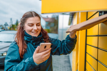 Caucasian woman putting parcel to cell of automatic post terminal and showing smartphone with delivery app. 