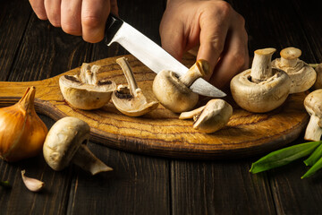 The cook cuts Agaricus mushrooms on a cutting board. Close-up of a chef hands with a knife. Peasant...