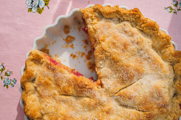 top down view of rhubarb pie with missing slice, pink tablecloth with blue roses
