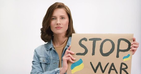 Portrait of young dark haired woman with stop war banner in hands protesting against russian attack in Ukraine. Glory to Ukraine and support concept.
