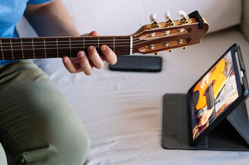 Adult man studying guitar online with tablet at home.