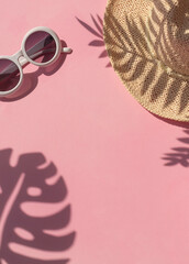Stylish summer vacation concept frame with straw hat, retro sunglasses and tropical leaves shadows on the pink background. Copy space