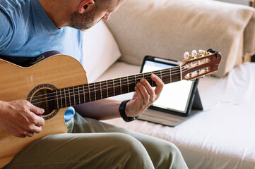 Adult man studying guitar online with tablet at home.