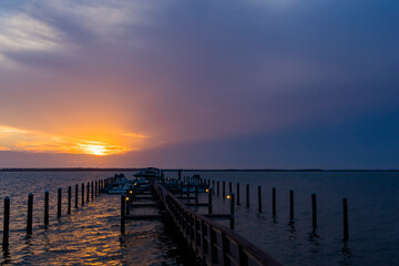 Fototapeta na wymiar A purple sunset looking down a dock that has small lights.