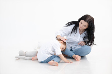 Woman and boy sitting together on floor, white background. Hugging, mother care. Autism spectrum...