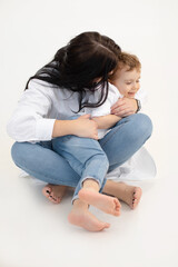 Vertical of black haired woman and little boy, hugging, having fun together. White background. Cuddling and sitting