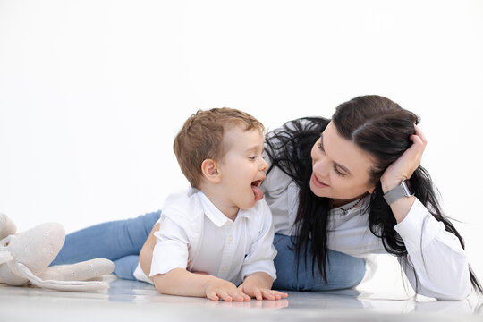 Black haired woman teacher and little boy showing tongue, lying on floor. Logopedics, early development, speech therapy