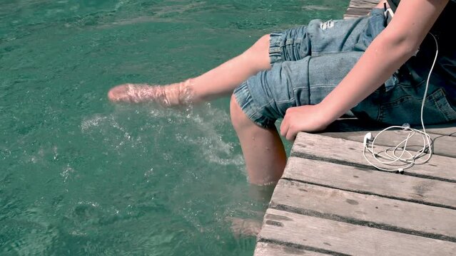 Junge sitzt am Badeteich, Pool und plantscht mit den F&uuml;&szlig;en im Wasser