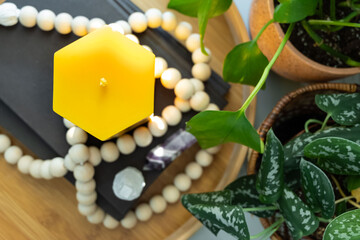 A tall hexagonal shaped beeswax candle is displayed with crystals, beads, and a plant. Birds eye view.