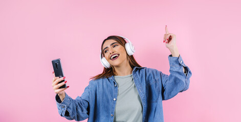 portrait of hispanic young woman with headphones, dancing and listening music on pink background in Mexico Latin America	