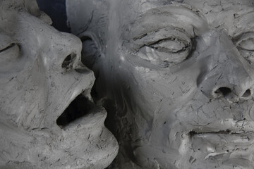 Female face in clay next to male face. Couple of head and face sculptures. Art work in process of...