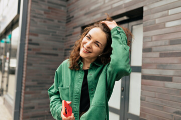 Lovely charming smiling girl with curls is wearing green jacket is happy smiling while spends time outdoor in warm sunny day