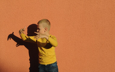 Boy playing in shadow theater, making crocodile on orange color background. Child makes shadows outdoors.