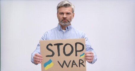 Portrait of middle aged bearded man raising cardboard banner with phrase Stop war while standing in studio over white background. European activist supporting Ukraine during war.