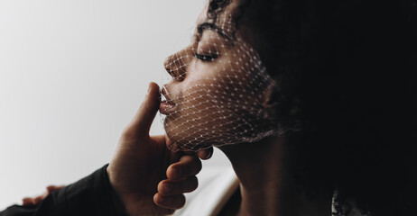 Creative photo. A man's hand holds the face of an african american woman with curly hair with a mesh on her face