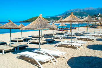 Straw beach umbrellas and comfortable sun loungers on clean sand and pebble beach. Himare. Albania.